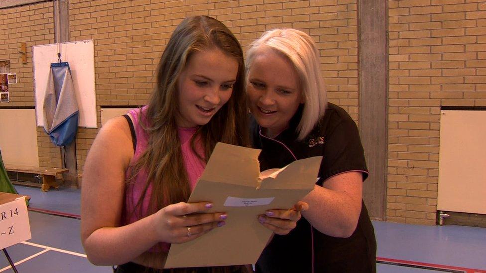 Abby and her mother look at a page of exam results in a school hall.