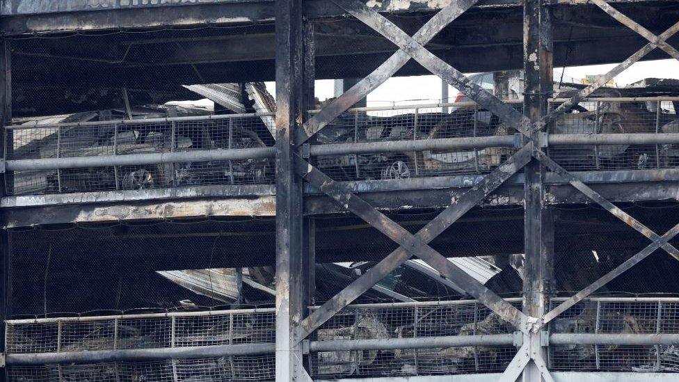 Burnt out cars can be seen in the damaged car park.