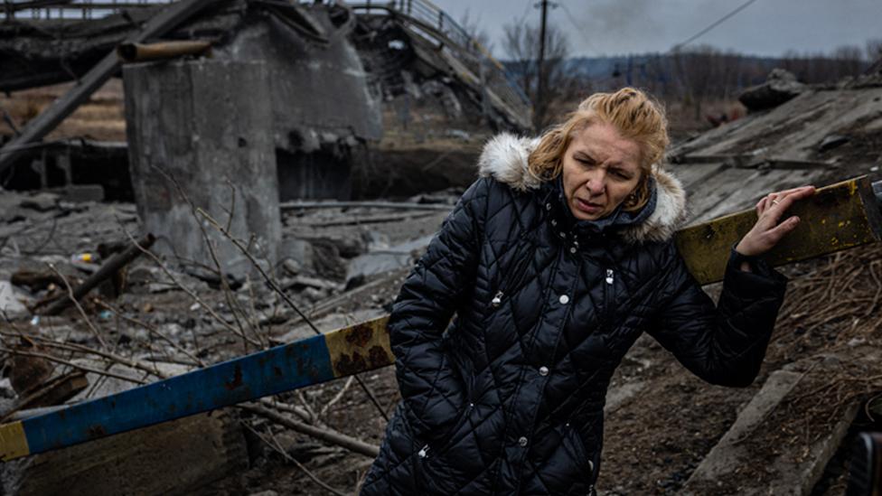 A woman takes a rest after crossing a destroyed bridge as she evacuates from the city of Irpin, northwest of Kyiv, on 7 March 2022 AFP