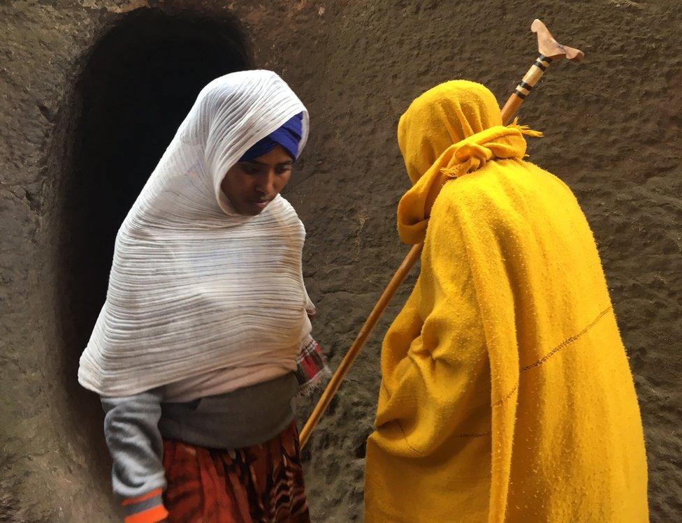 A pilgrim (left) passes a nun (right) in a subterranean tunnel carved