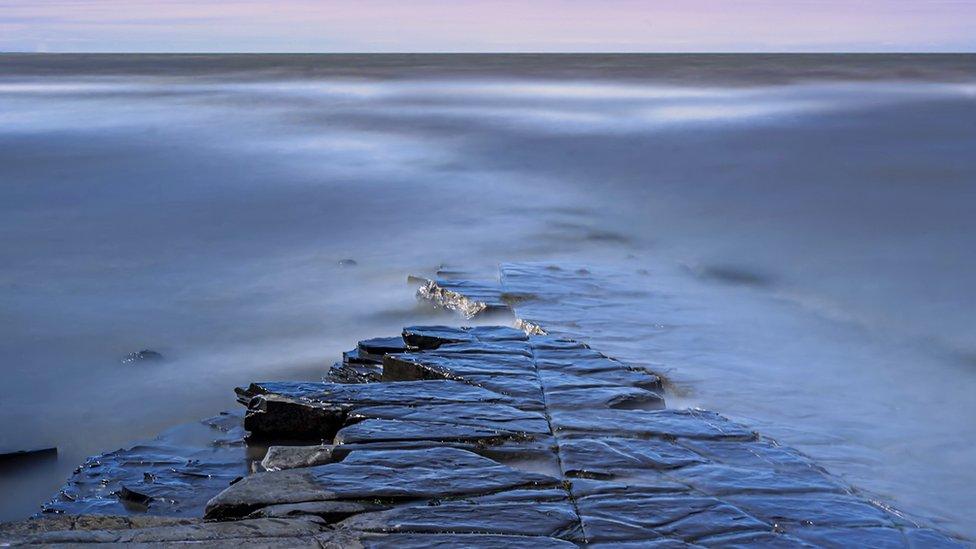 long exposure dawn coastal photography of rocks emerging from water.