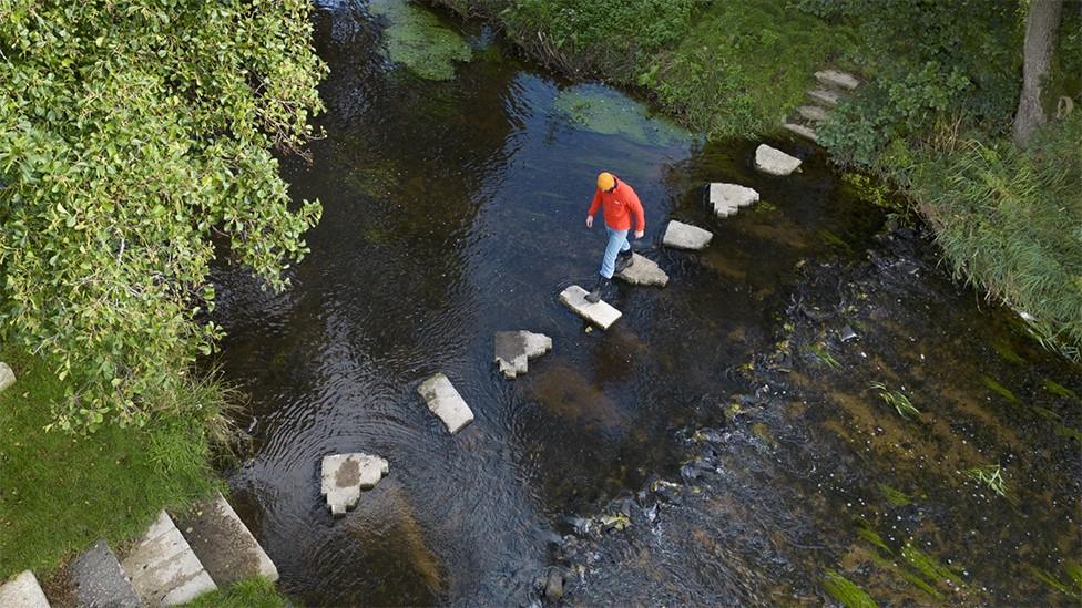 Man walking on stepping stones to cross river