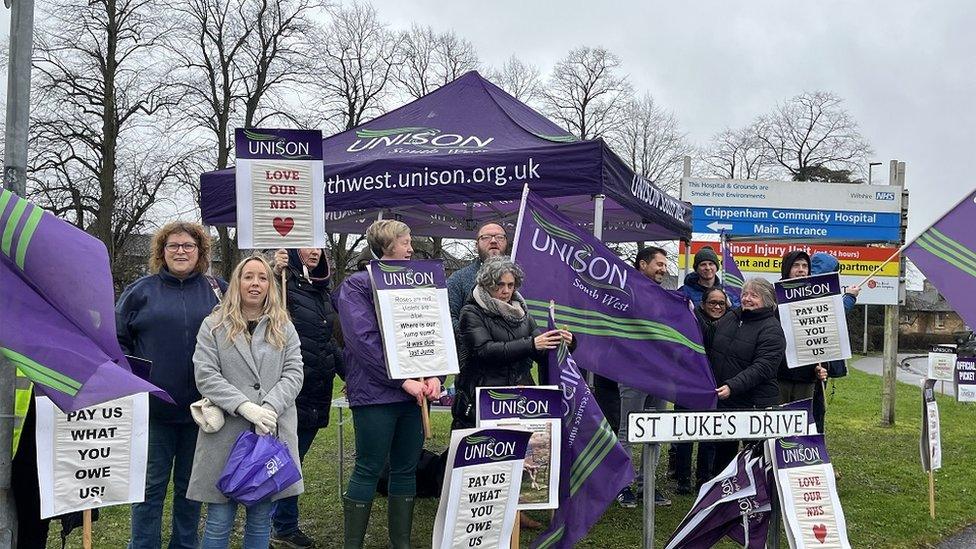 Staff holding signs and flags with a lot of purple outside a hospital sign