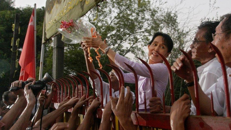 Myanmar"s detained opposition leader Aung San Suu Kyi holds a bouquet of flowers as she appears at the gate of her house after her release in Yangon on November 13, 2010. Myanmar"s democracy leader Aung San Suu Kyi walked free from the lakeside home that has been her prison for most of the past two decades, to the delight of huge crowds of waiting supporters. Waving and smiling, the petite but indomitable Nobel Peace Prize winner appeared outside the crumbling mansion where she had been locked up by the military junta for 15 of the past 21 years.