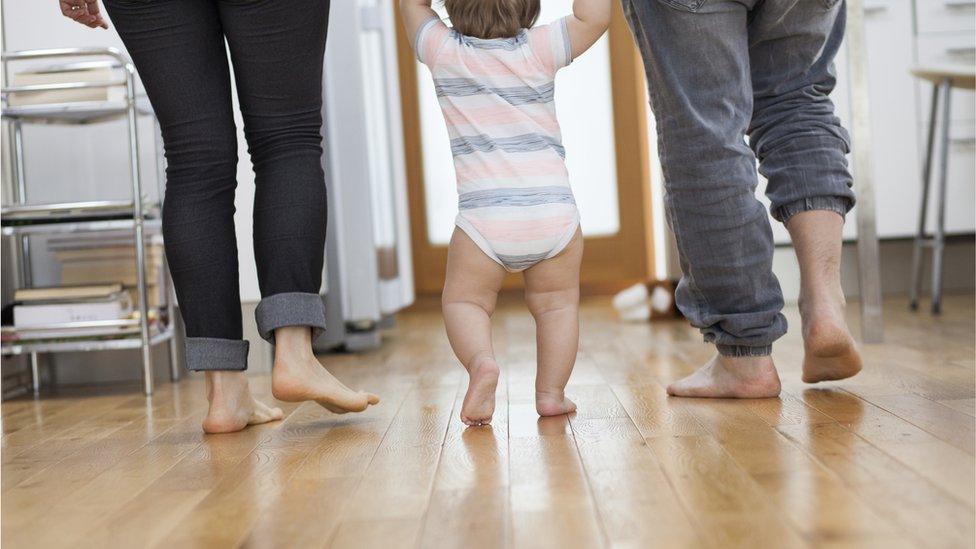 Mum and dad holding hands with walking baby