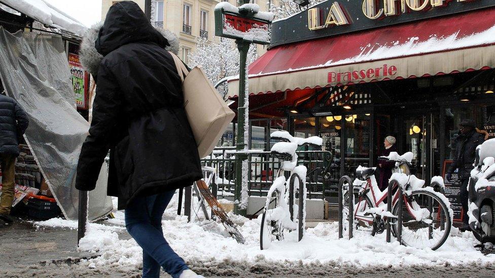 A woman crosses a snow-covered Parisian street by a metro station entrance