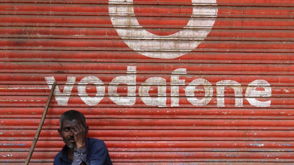 A man sits outside the downed shutters of a shop painted with a logo of Vodafone on its shutter in Mumbai, India on 24 February 2019