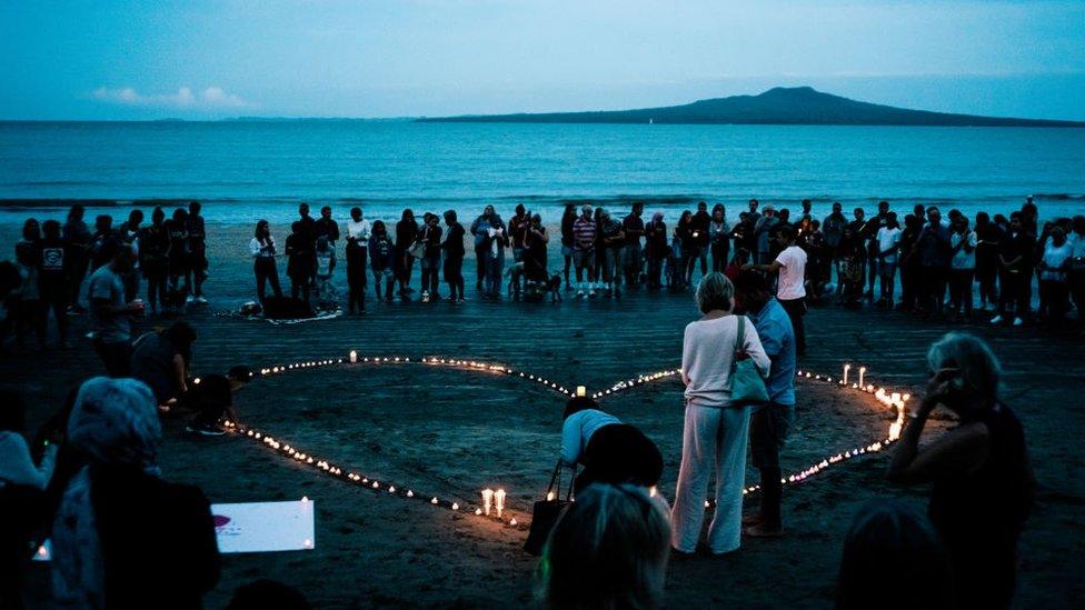 A vigil on a beach in Auckland with people standing around a heart-shape made from candles