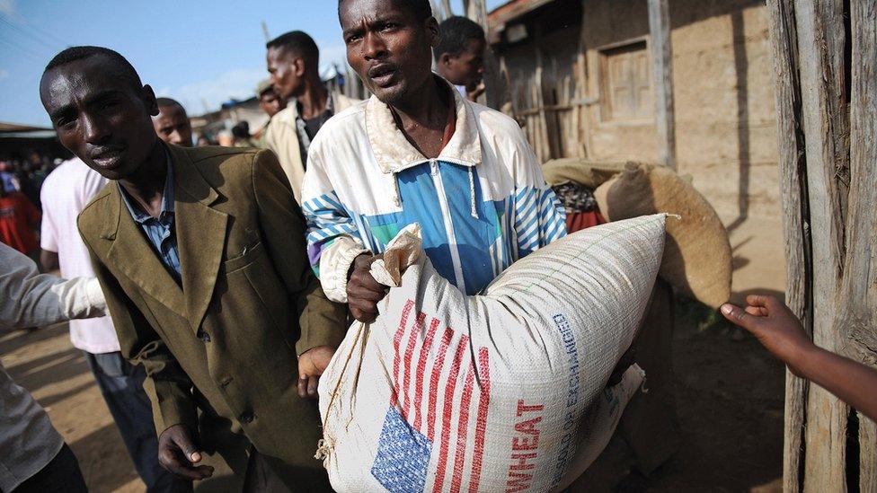 Two men carrying a bag of wheat branded with the US flag