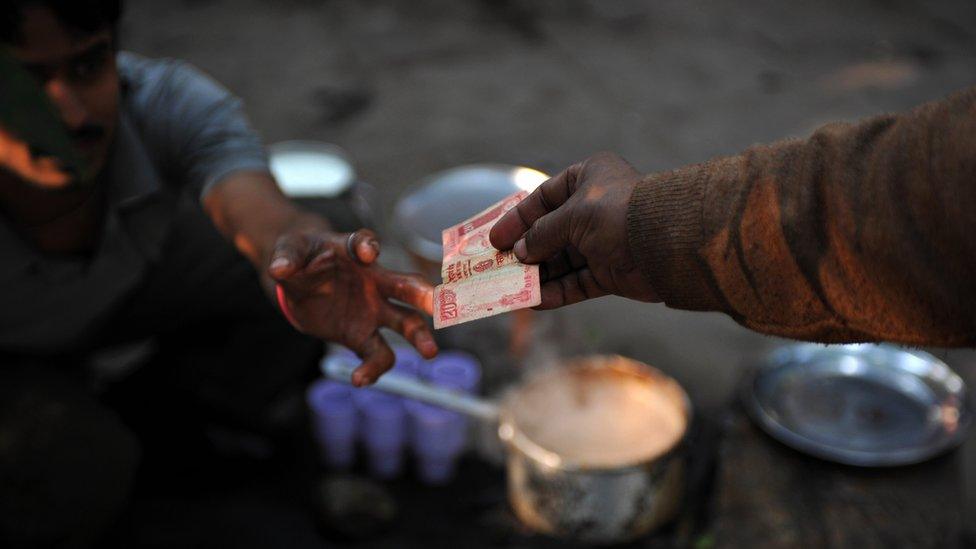 A tea seller in India accepts money from a customer