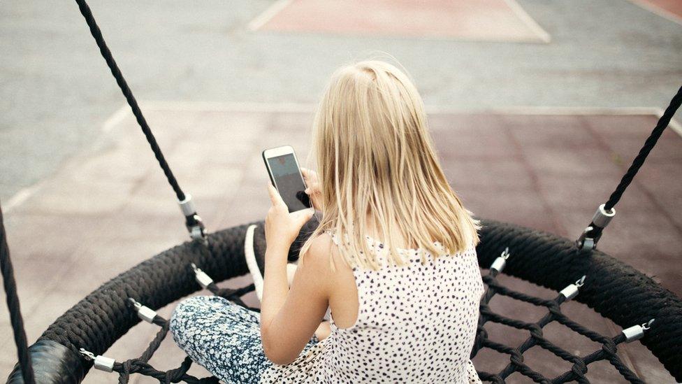 A young girl using a mobile phone while sat on a swing