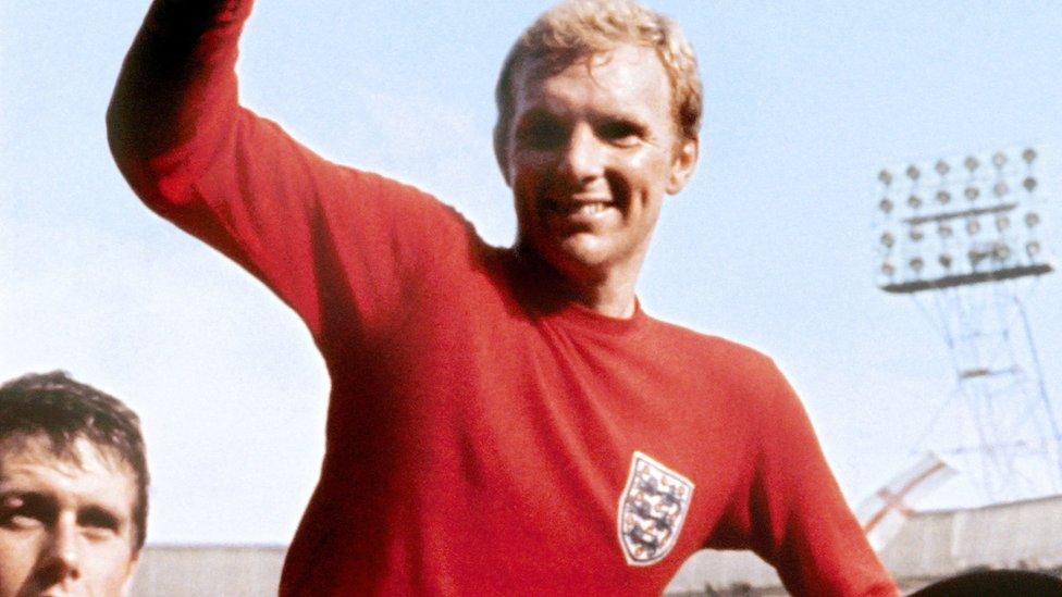 Sir Bobby Moore in the iconic red England shirt holding the World Cup trophy