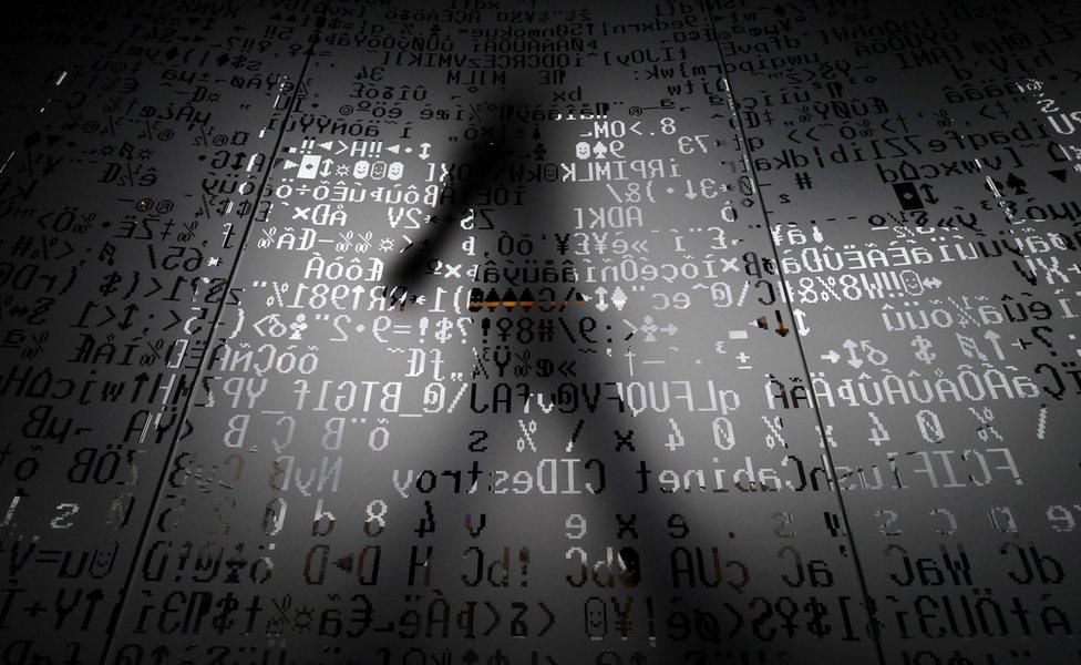 A silhouette of a man walking behind a glass wall with machine coding symbols at the headquarters of Internet security giant Kaspersky in Moscow