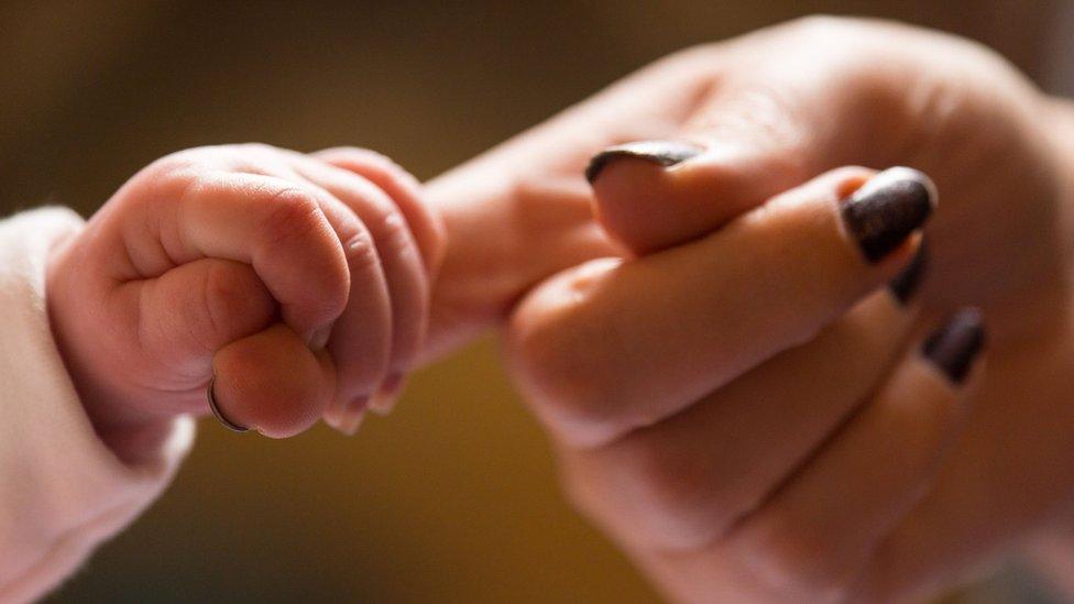 A baby holds onto an adult's finger