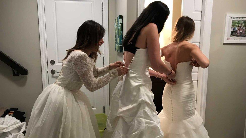 Three friends help each other into wedding dresses