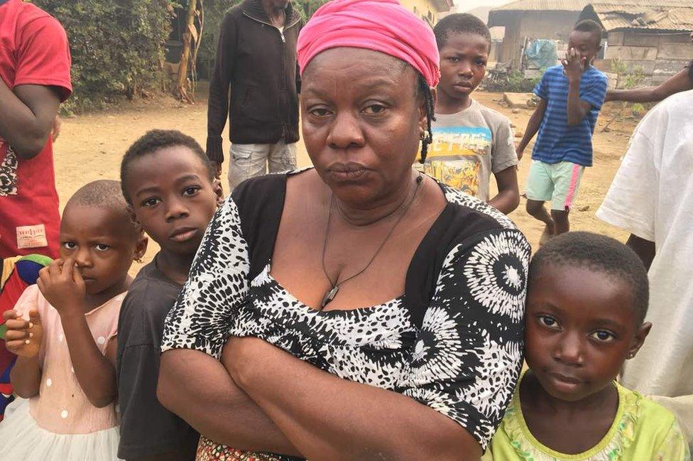 Regina crosses her arms in front of her, flanked on either side by young children