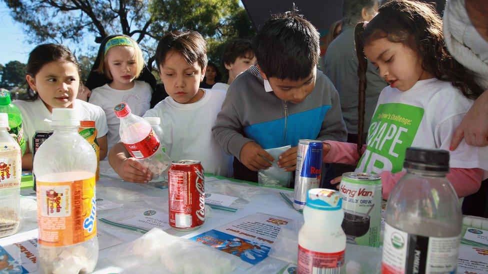 School children look at a display showing how much sugar is in soft drinks and juices