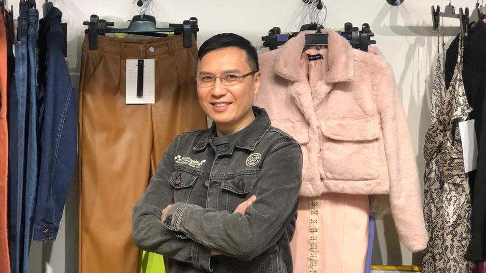 Johnny Tseng in front of fashion pieces he sells to UK labels including a pink furry coat and camel trousers