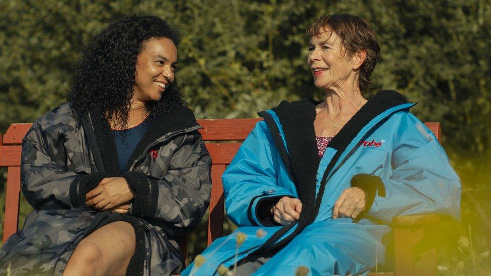 Young woman with long dark hair sits on a bench with an older woman with short hair