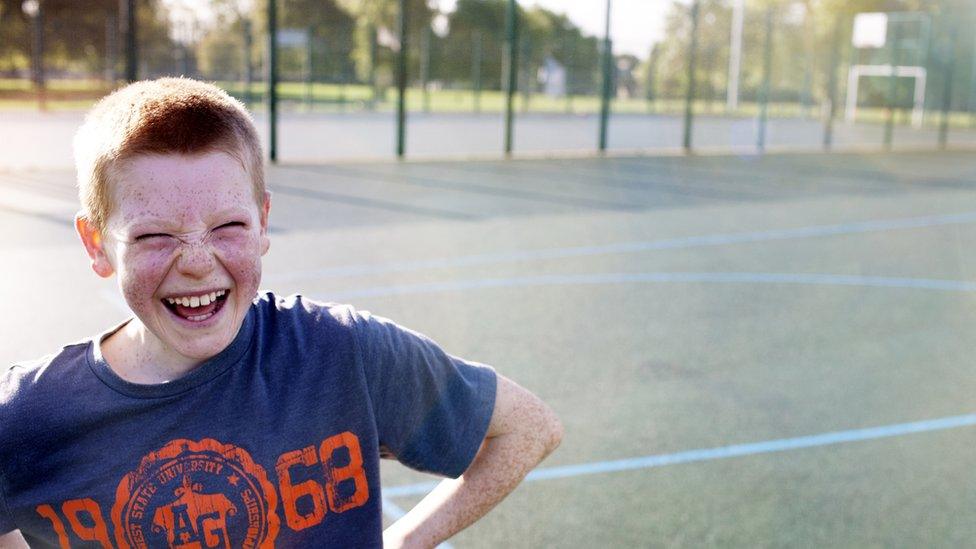 Young child laughing at the camera, on a football pitch