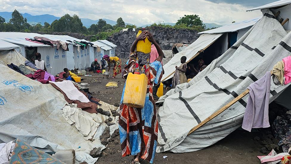 A woman carries cartons amid tents in the Bushagala camp, North Kivu province, DR Congo