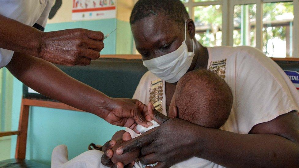 a baby receives a vaccine from malaria while being held by an adult