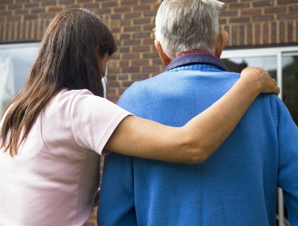 Home carer with arm round disabled man's shoulders