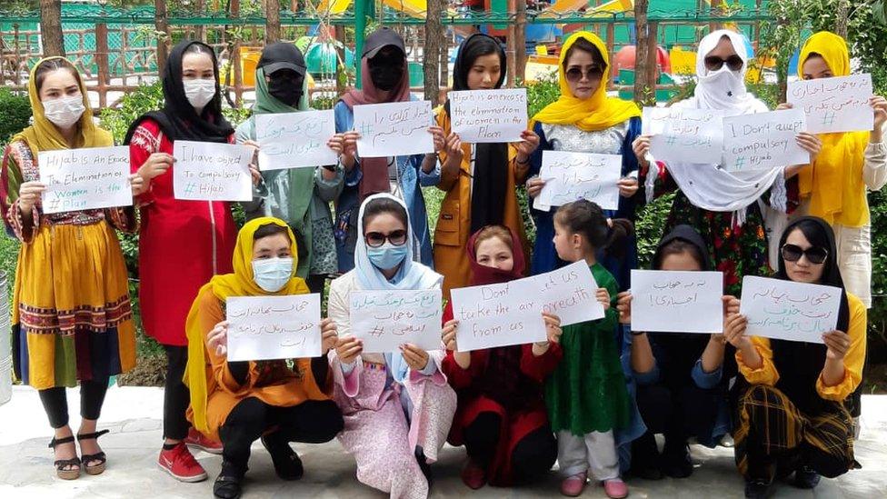 Women in Afghanistan hold signs to object being ordered to cover their faces in public by the Taliban