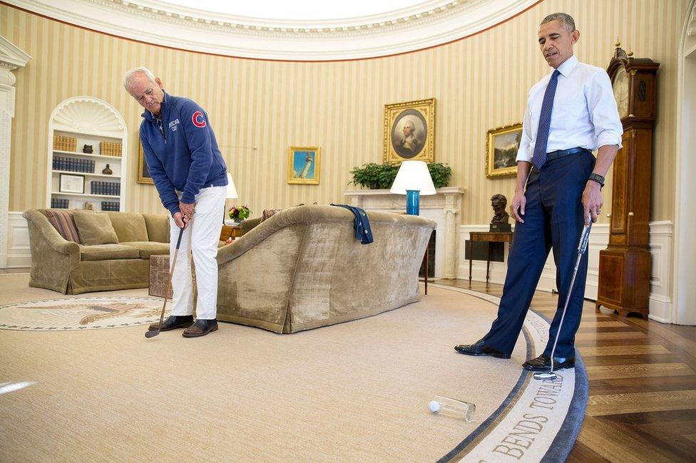 Bill Murray, left, putts a golf ball into a drinking glass in the Oval Office, as Barack Obama looks on