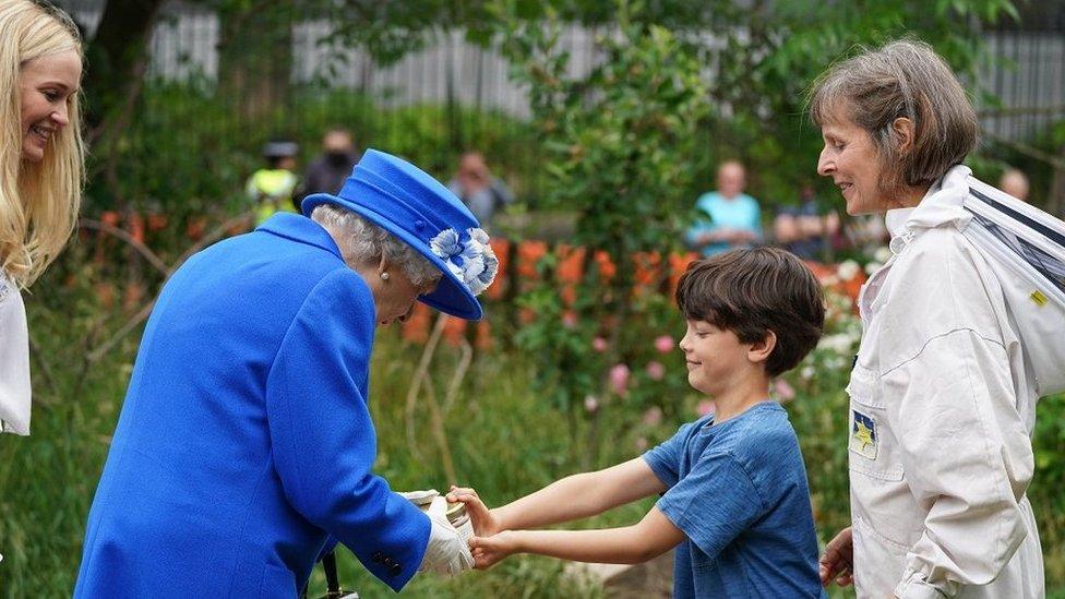 The Queen taking a pot of honey from a boy