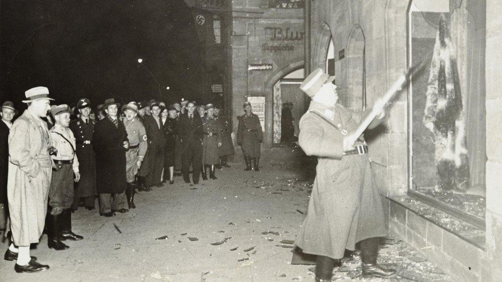 People watch as a Nazi official attacks a Jewish business