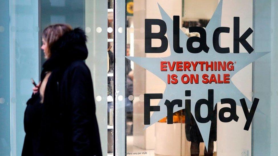 Shoppers pass a promotional sign for 'Black Friday' sales discounts, outside a store on Oxford Street in London, on November 26, 2019