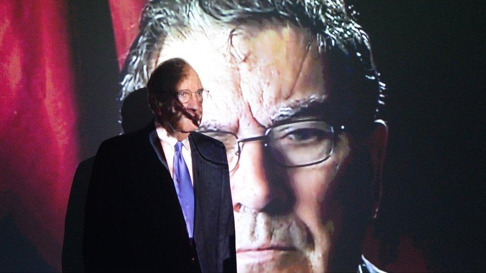 Former US Senator George Mitchell standing in front of an image of John Hume