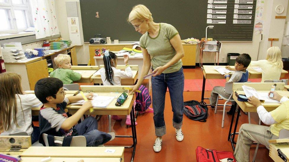 A teacher hands rulers to children in a primary school in Vaasa, Finland