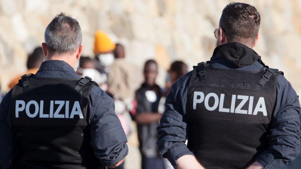 Policemen look on as migrants from the Rise Above ship arrive at the port of Reggio Calabria