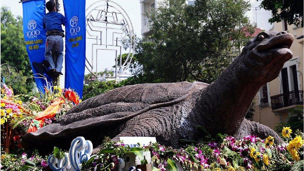 A worker installs banners marking the millennium anniversary of Hanoi next to a model of the capital's Hoan Kiem lake legendary turtle on display in the centre of Hanoi on 30 September 2010