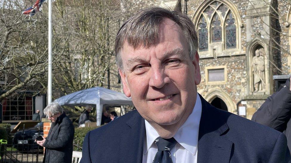 Man with short grey hair and wearing a tie stands in a street