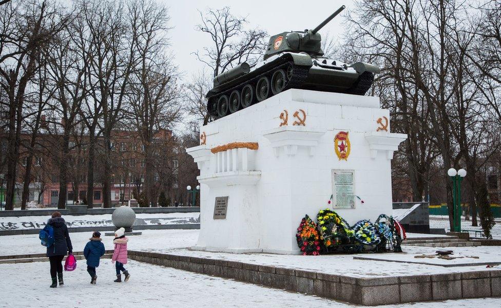 A mother and her two children walk past a Soviet world war two memorial in snowy Kamyanets-Podilskyi