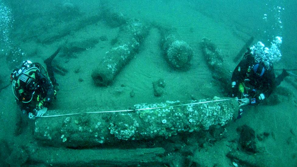 Drivers measuring a cannon underwater