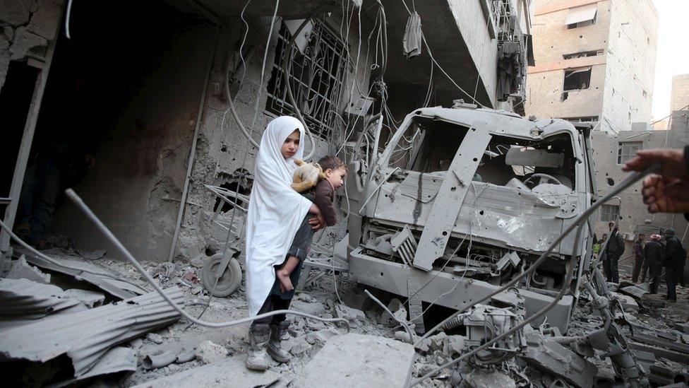 A girl carries a baby at the site of what activists said was a government air strike in Douma, in the eastern suburbs of Damascus (10 January 2016)