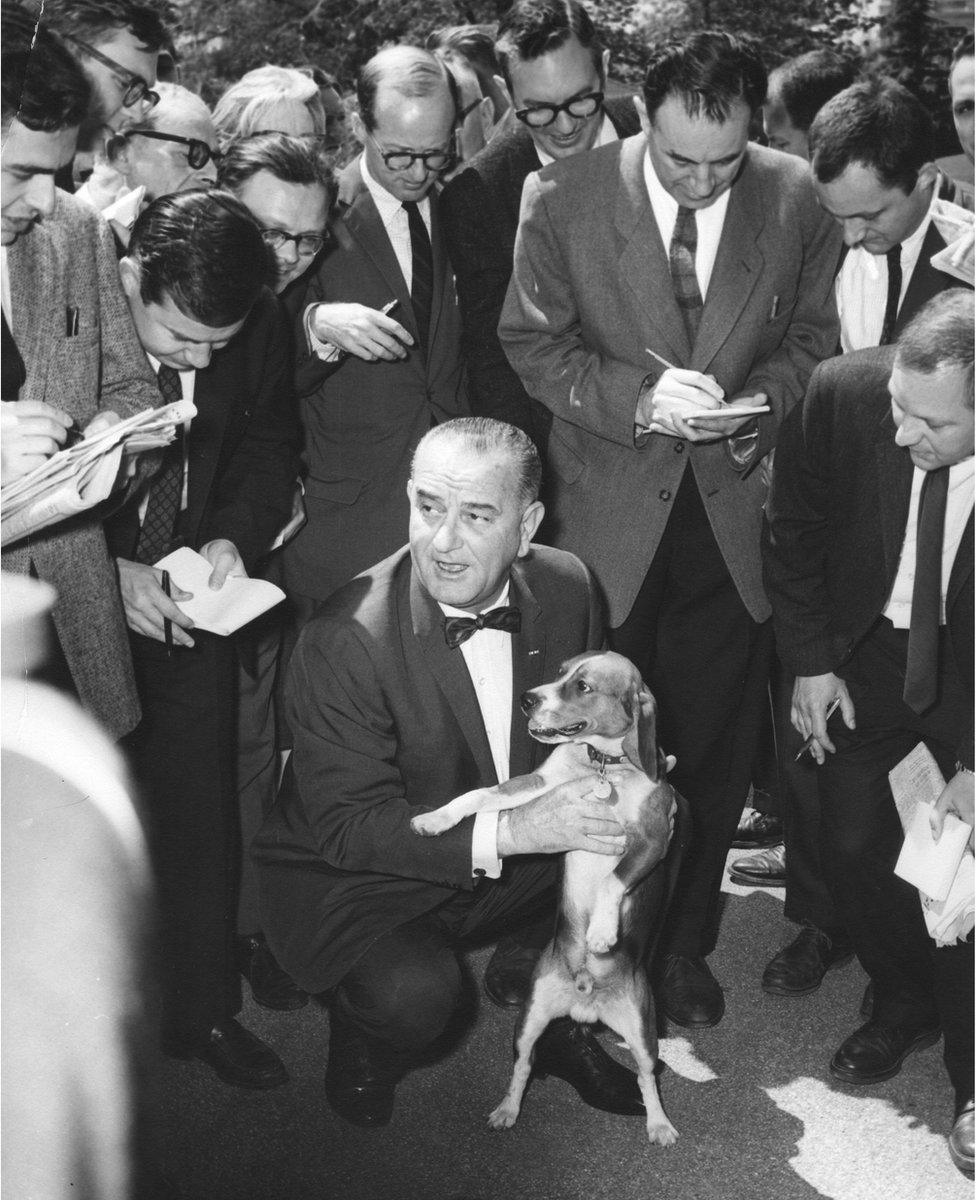 President Lyndon Johnson holds a beagle dog whilst speaking to a group of journalists