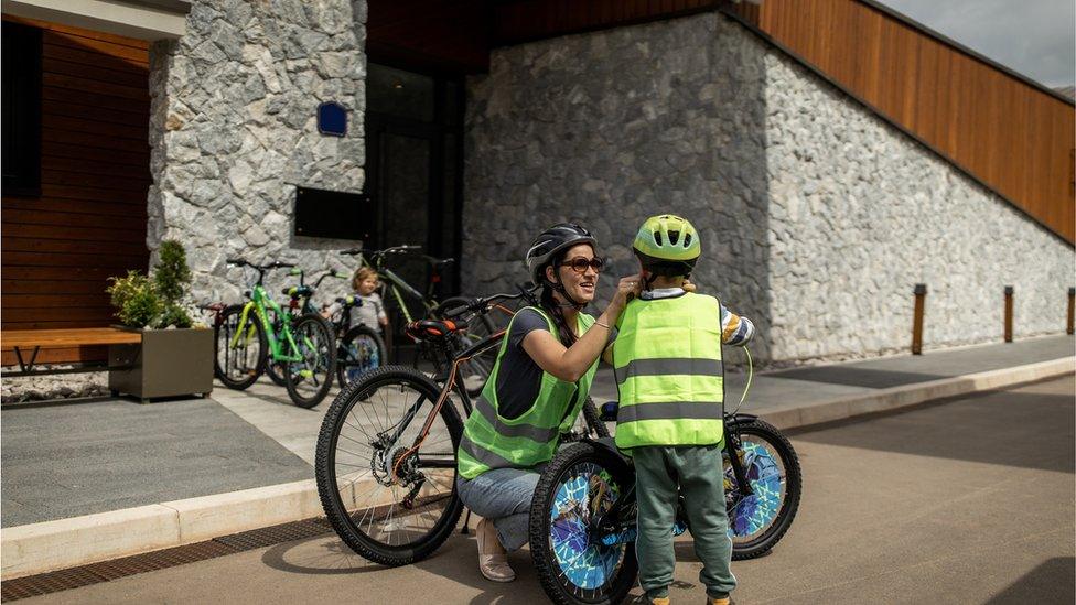 Young woman wearing cycling helmet and waistcoat and preparing her son for bike riding