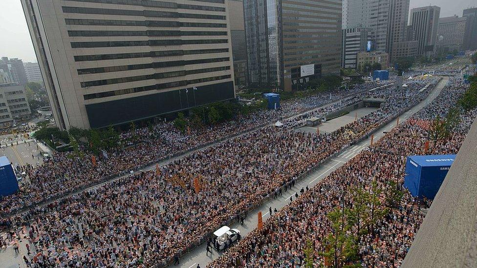 Thousands of South Koreans watch as Pope Francis drives through central Seoul in August 2014