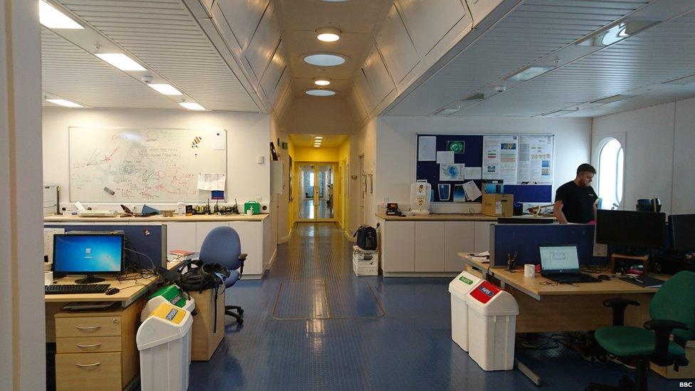 A view down a long corridor, with tables either side and a man standing on the right