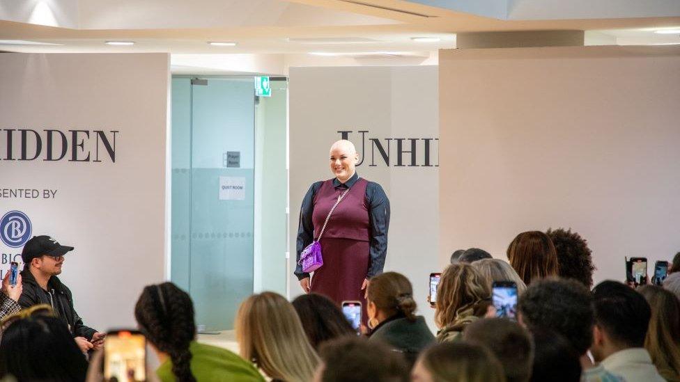 Laura Mathias in purple dress and dark top walking a catwalk at London Fashion Week