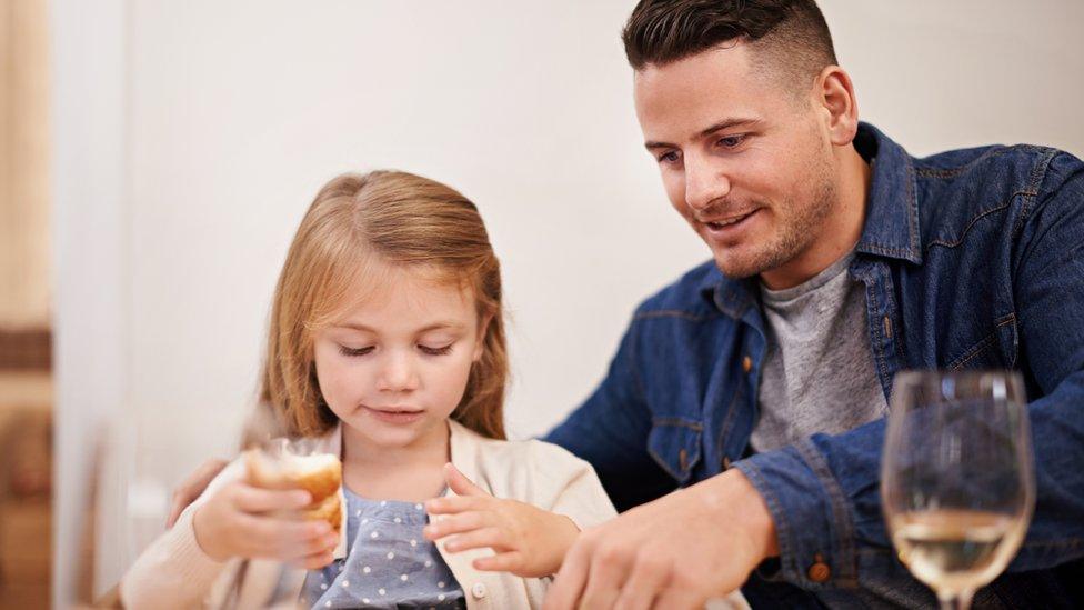 Stock image of father and daughter at table with glass of wine next to man