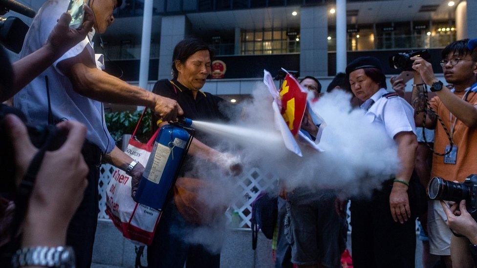 Security guard (L) extinguishes a burning portrait of Chinese leader Xi Jinping held by pro-democracy activist Lui Yuk-lin (2nd L) in Civil Square outside the Central Government Complex after attending a protest march by thousands in Hong Kong on July 1, 2018