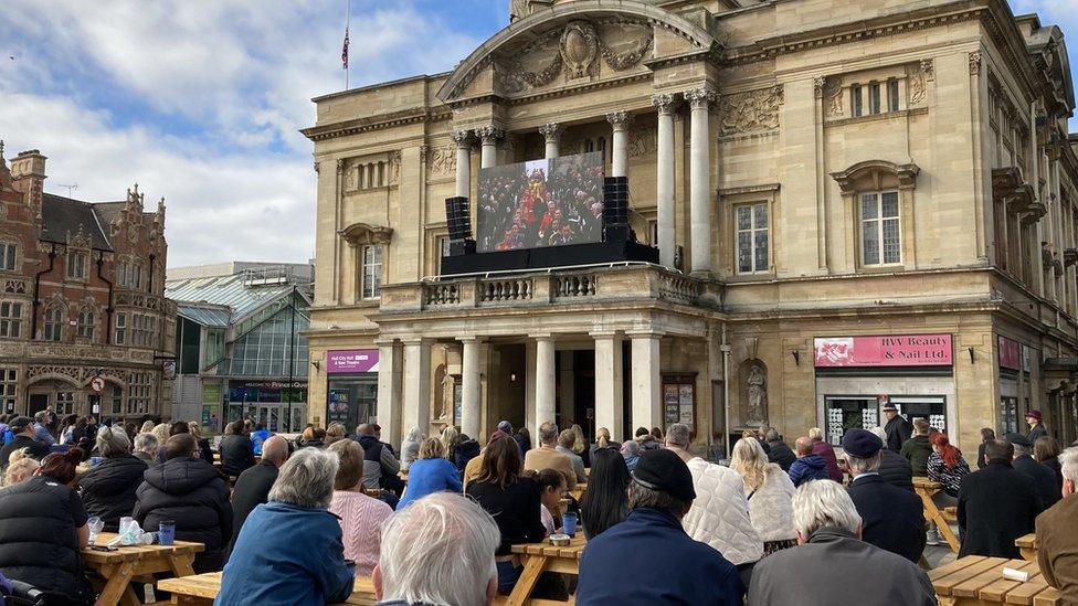 People sitting watching funeral broadcast