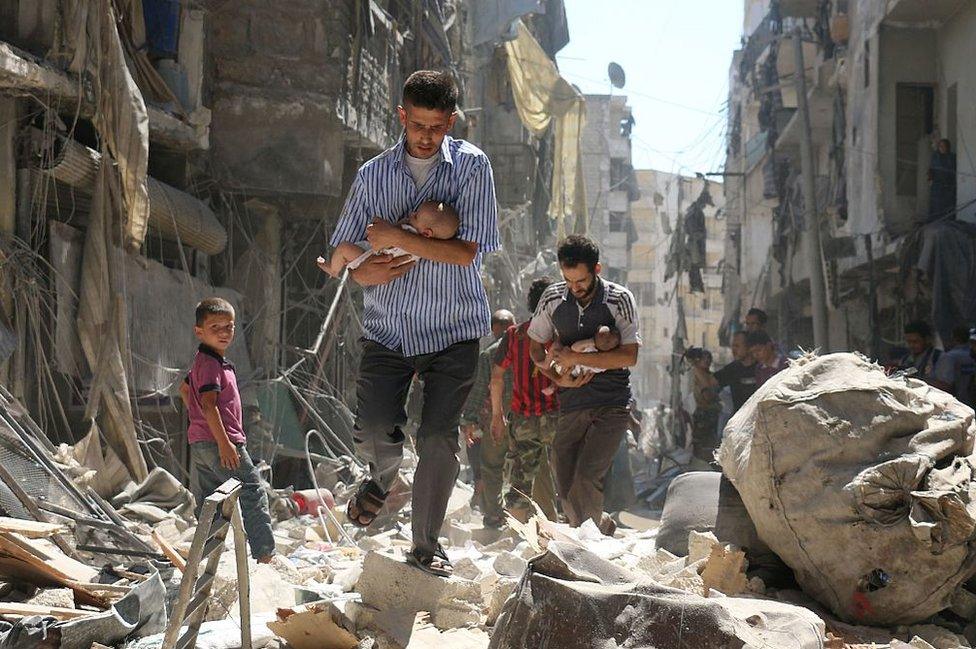 Syrian men carrying babies make their way through the rubble of destroyed buildings following a reported air strike on the rebel-held Salihin neighbourhood of the northern city of Aleppo on 11 September 2016.