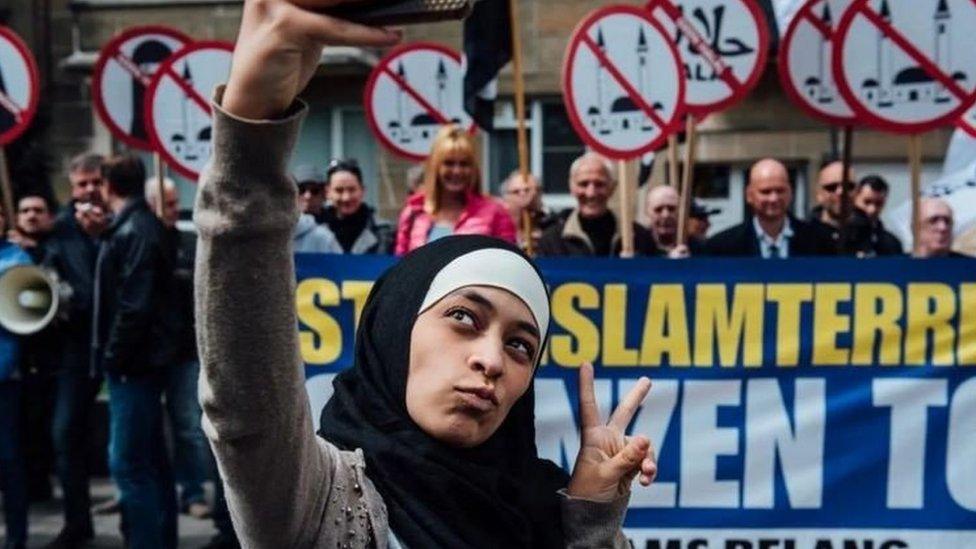 Photo of Zakia Belkhiri taking a selfie with Vlaams Belang protesters in the background